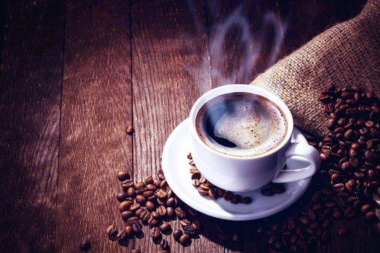 Coffee beans and a steaming cup on a rustic wooden table
